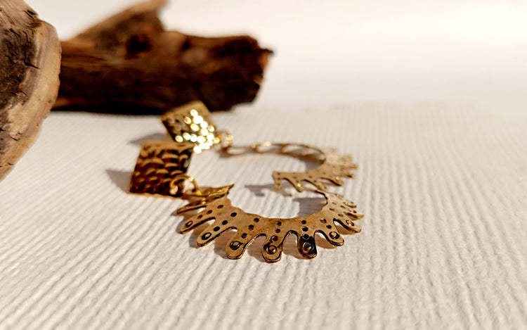 Złote kolczyki w kształcie słońca z ażurowym wzorem na białym tle z drewnianymi elementami dekoracyjnymi