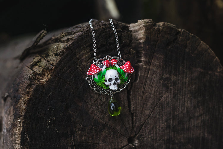 naszyjnik z czaszką ozdobioną czerwonymi grzybami i zielonymi kryształami na ciemnym tle